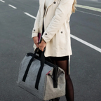 Lieblingstasche Allrounder M grey travel bag with black handles held by a woman in a beige trench coat