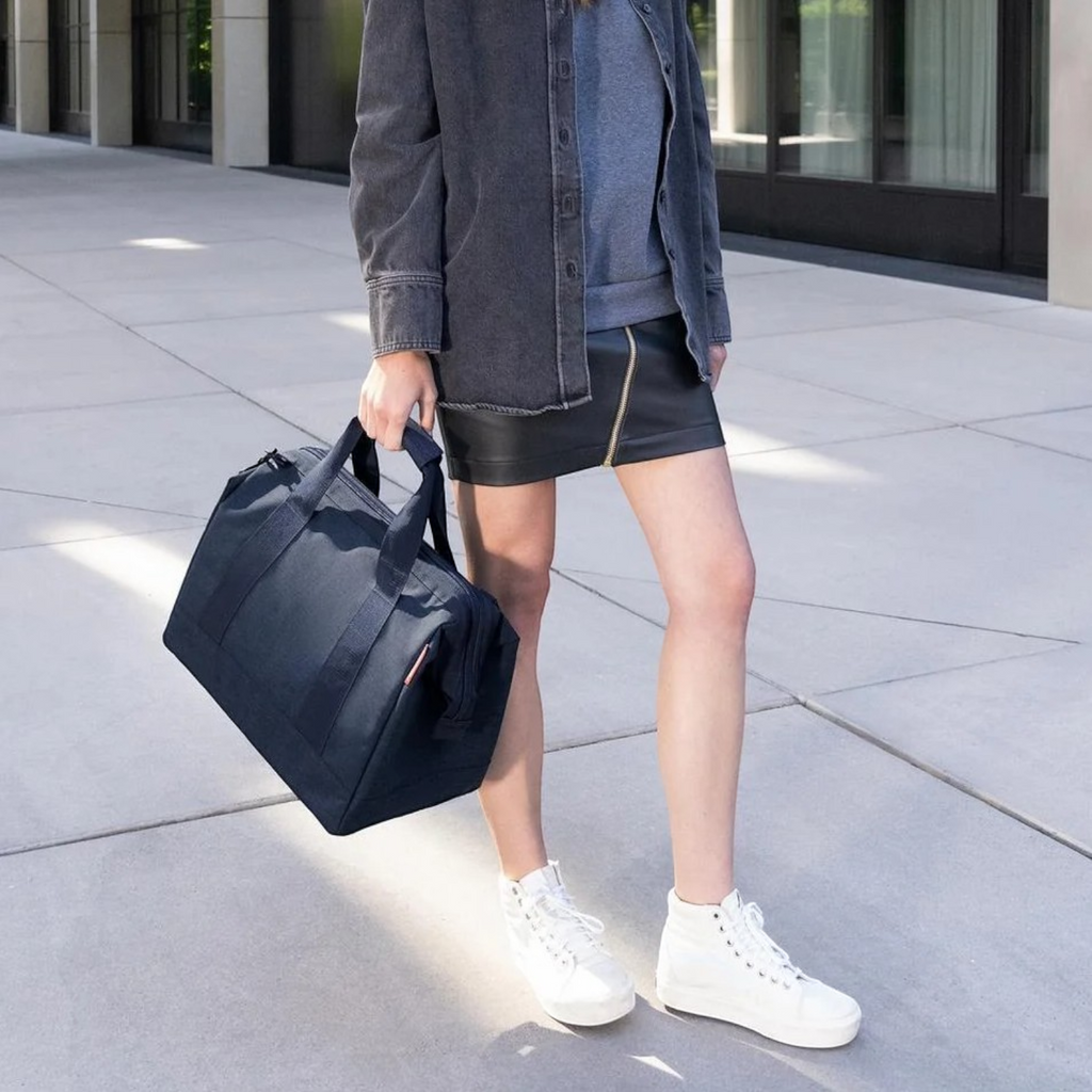 Lieblingstasche Allrounder M navy blue travel bag held by a woman wearing a dark denim jacket and black skirt