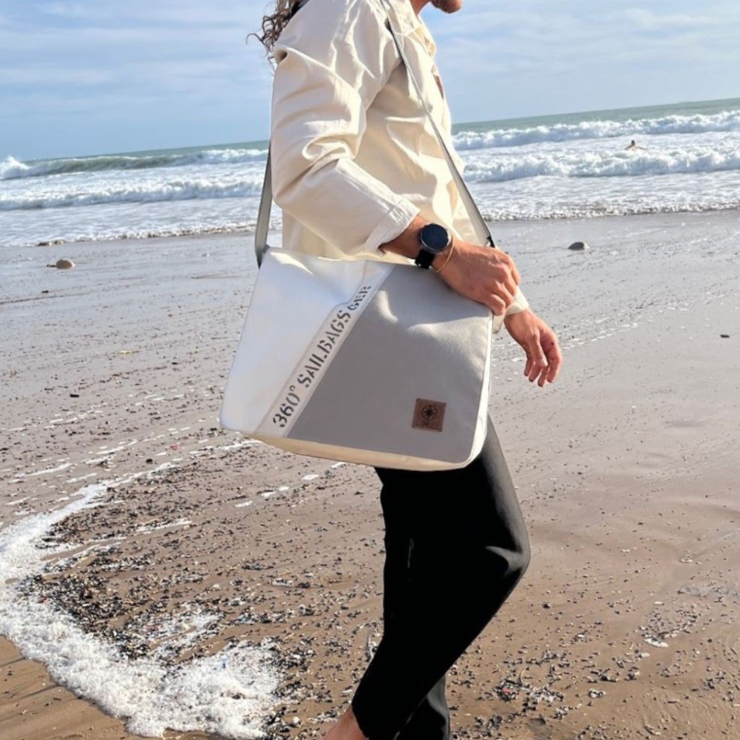 Lieblingstasche Barkasse shoulder bag made from recycled sailcloth with unique stitching, worn by a man on the beach.