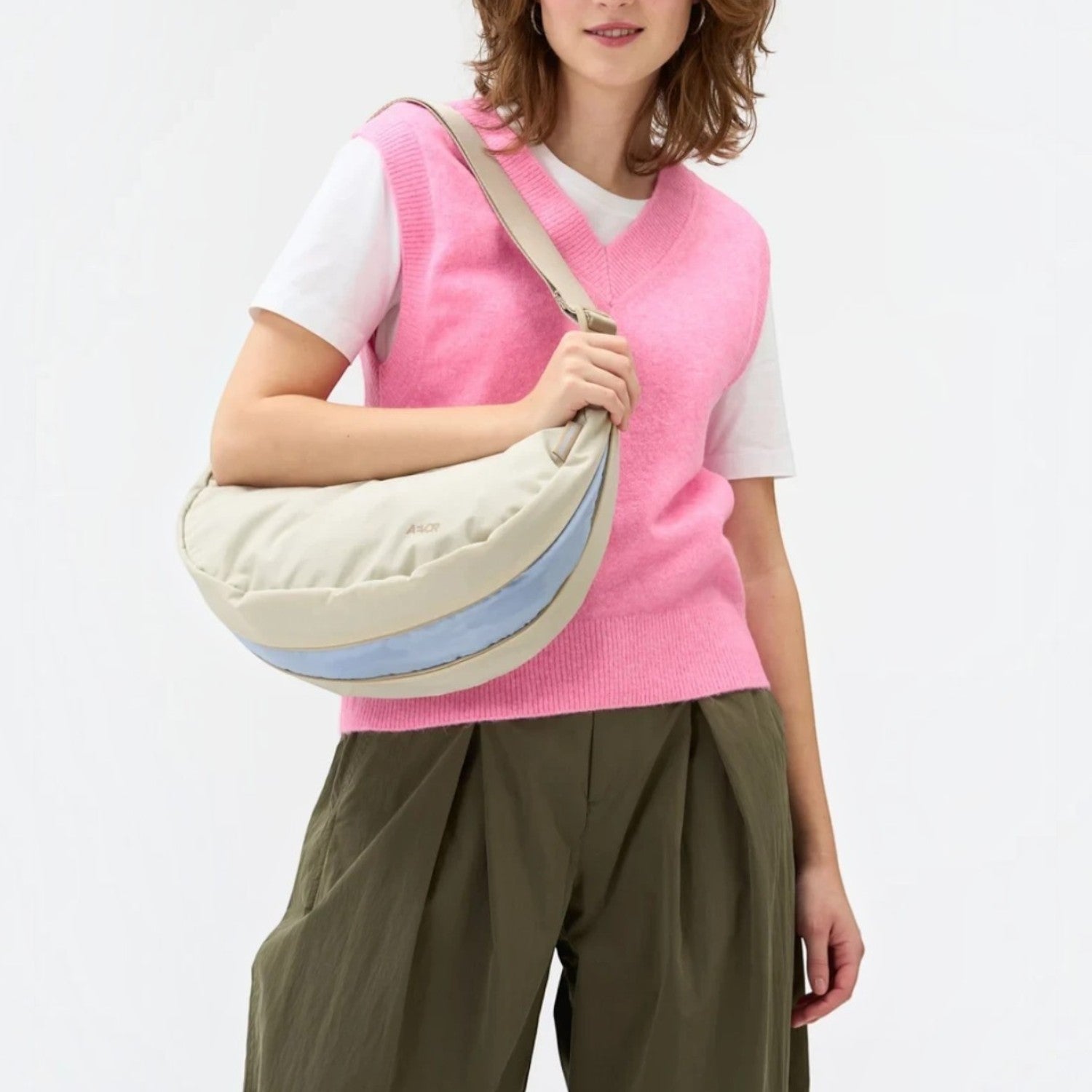 Lieblingstasche beige and light blue water-resistant sling bag worn crossbody by a woman in a pink sweater vest