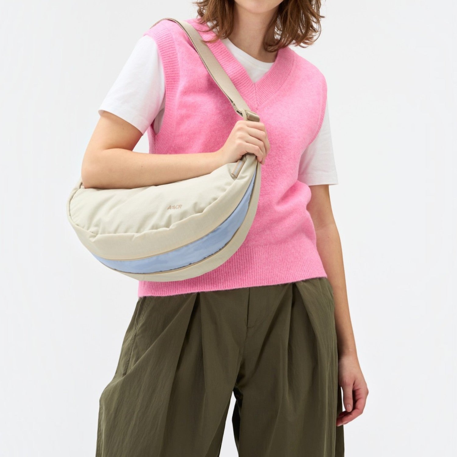 Lieblingstasche beige crescent sling bag with a light blue accent stripe worn by a woman in a pink sweater vest