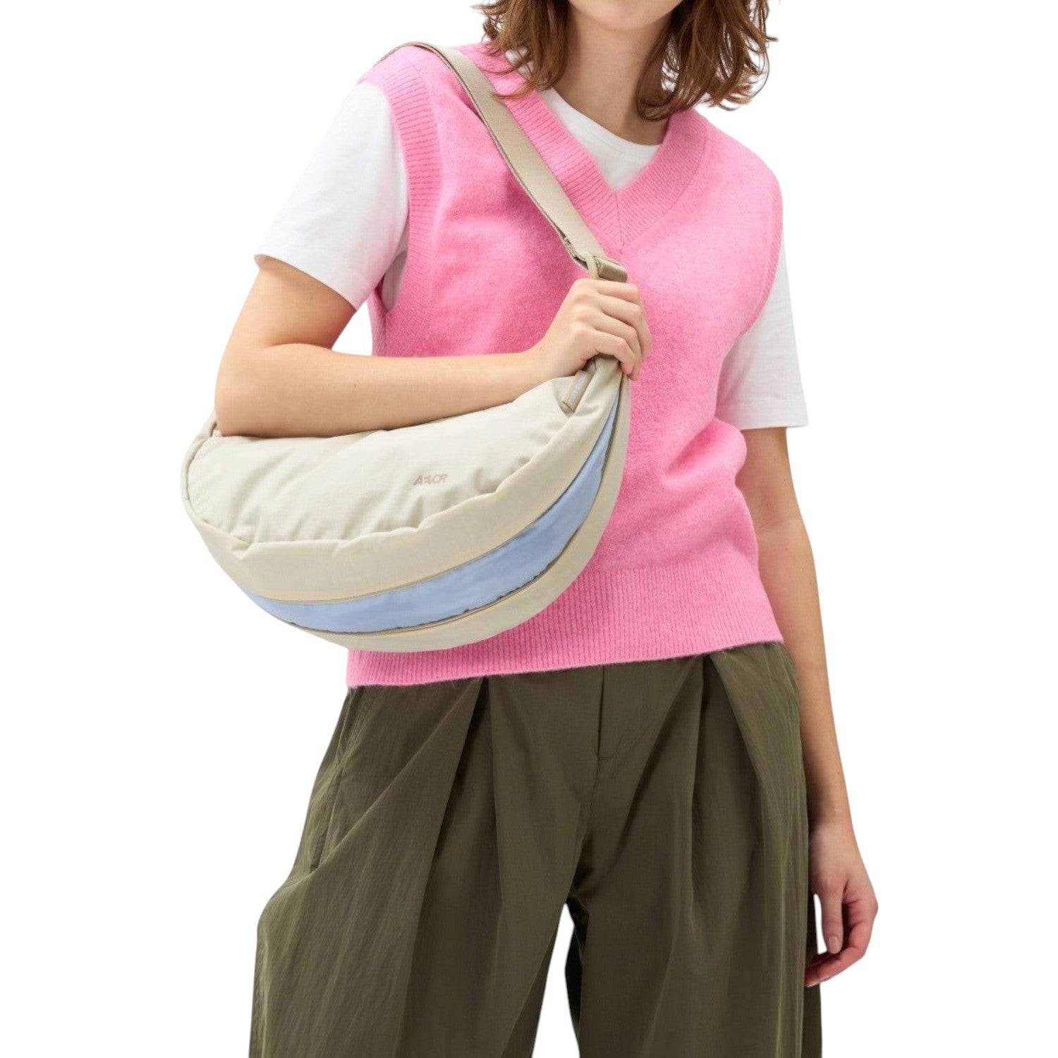 Lieblingstasche beige crescent sling bag with a light blue accent stripe worn by a woman in a pink sweater vest