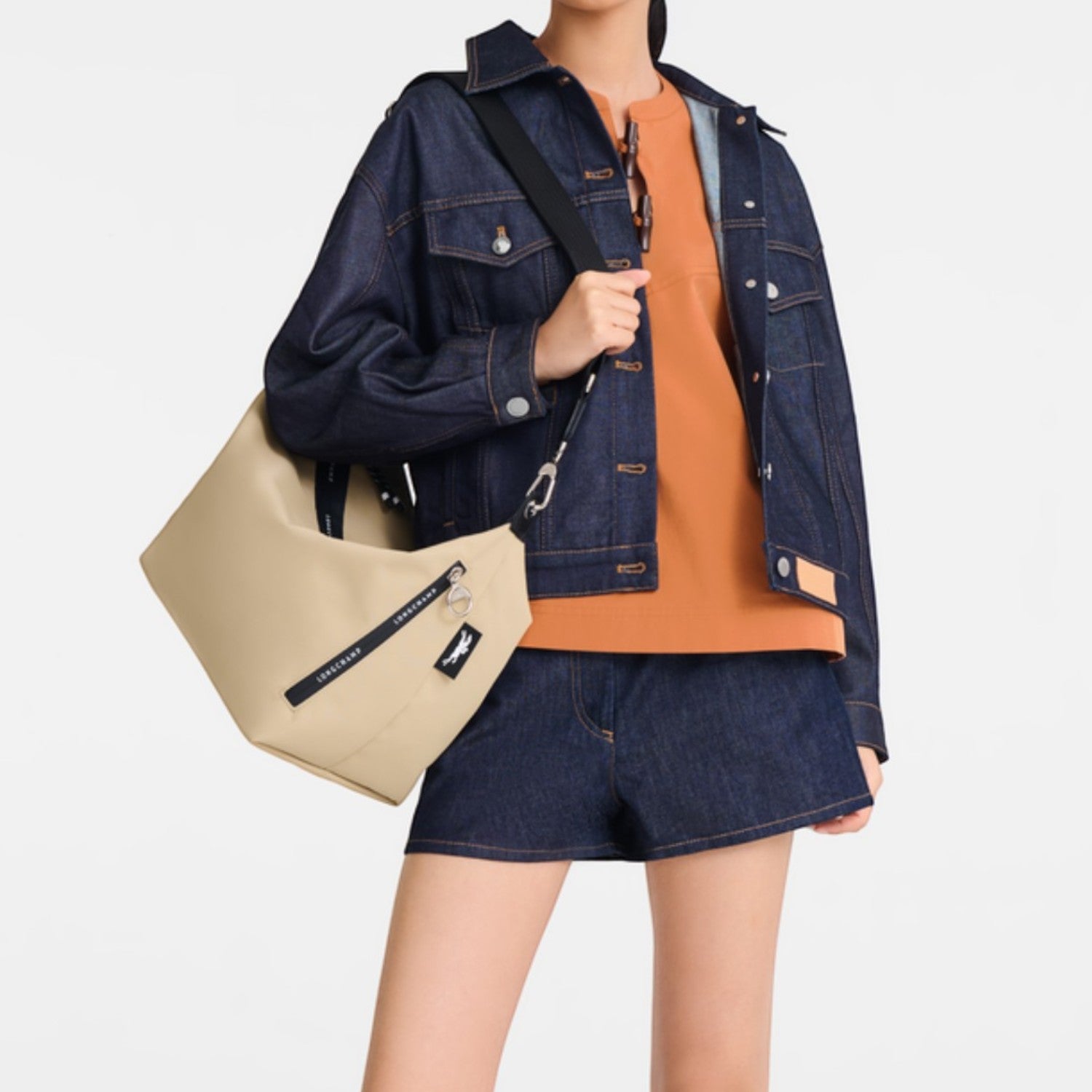 Model wearing a beige Lieblingstasche Le Pliage Energy crossbody bag with black logo strap and denim outfit