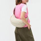 Lieblingstasche beige water-resistant sling bag worn crossbody by a woman in a pink vest and green trousers
