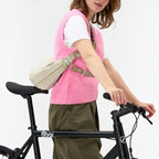 Lieblingstasche beige water-resistant sling bag worn crossbody by a woman on a bicycle for urban commuting.