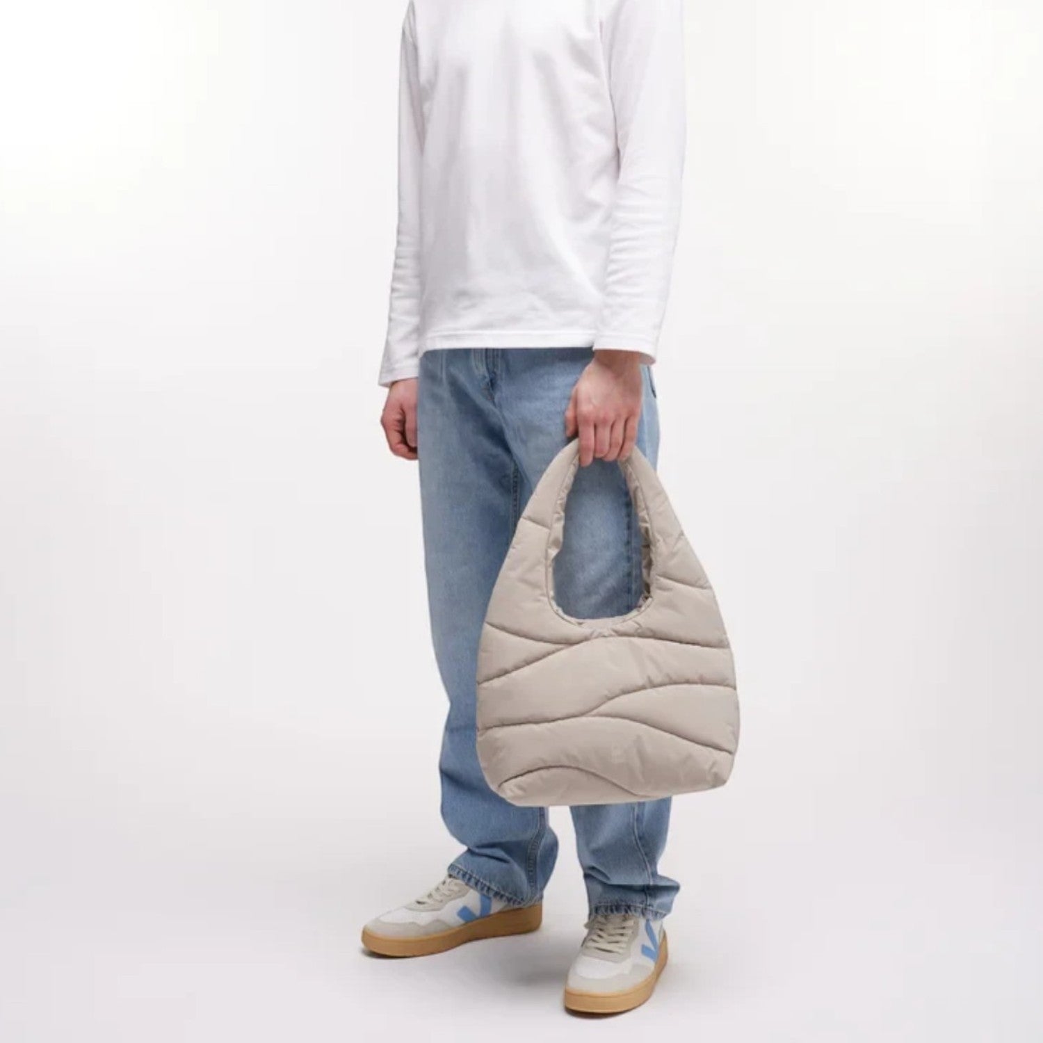 Lieblingstasche beige wavy puffer shoulder bag held by a man in a white long-sleeve shirt and light blue jeans