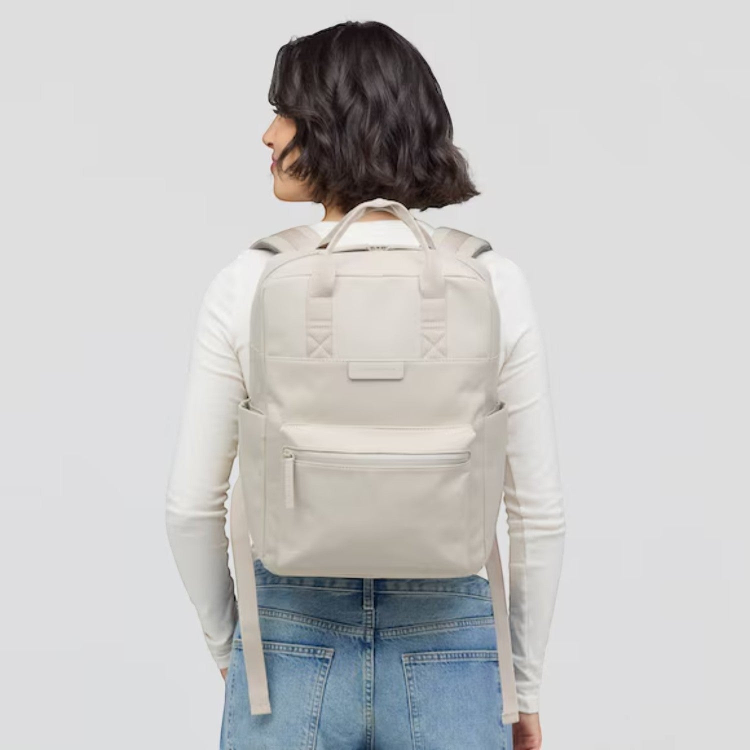 Woman wearing a beige Lieblingstasche Bergen Pro backpack with padded straps and front pocket, back view