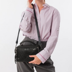 Lieblingstasche black Anekke cross-body bag with laser-cut details and top handle worn by a woman in a lilac shirt