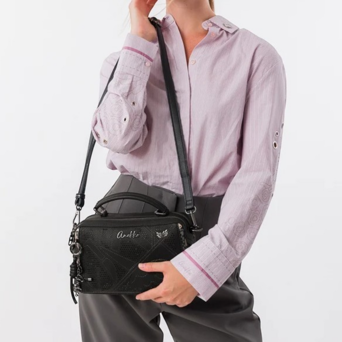 Lieblingstasche black Anekke cross-body bag with laser-cut details and top handle worn by a woman in a lilac shirt