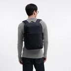 A man wearing a black Lieblingstasche Commuter Pack backpack against a plain white background.