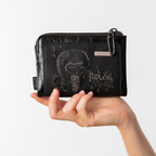 Lieblingstasche black wallet with embossed girl graphic and Relish the Moment text, held in a hand
