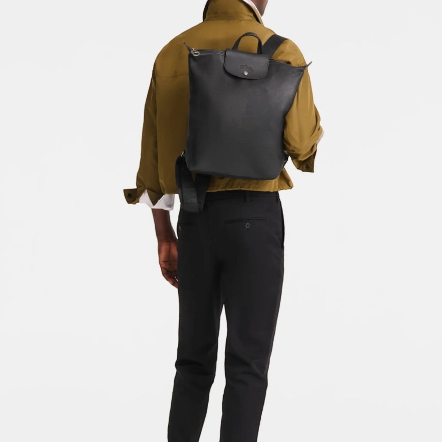 A man wearing a black Lieblingstasche Le Pliage Xtra Rucksack M on his back, styled with an olive jacket and black trousers.