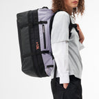 Model wearing a Lieblingstasche black and light purple duffel pack with adjustable straps on a white background