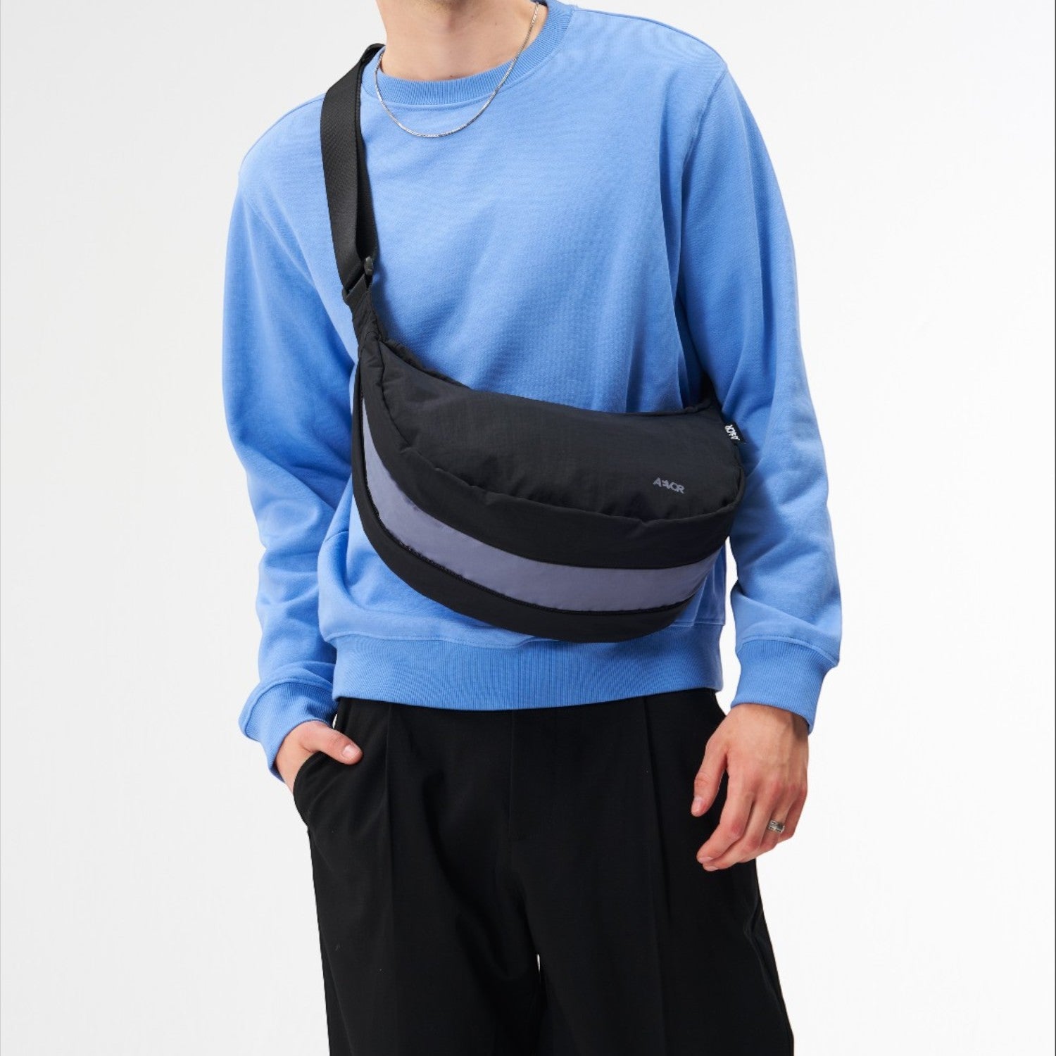 Lieblingstasche black sling bag with a grey reflective stripe worn across the chest by a man in a blue sweatshirt