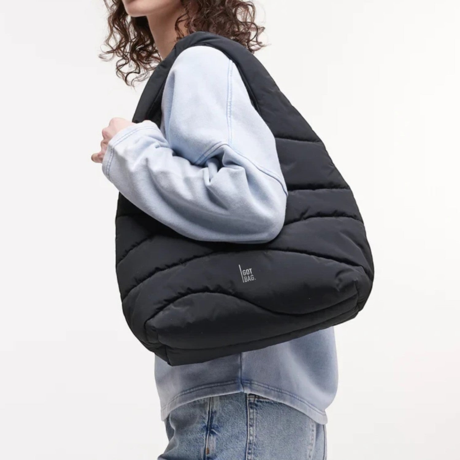 Lieblingstasche black wavy puffer shoulder bag worn by a woman in a light blue sweatshirt