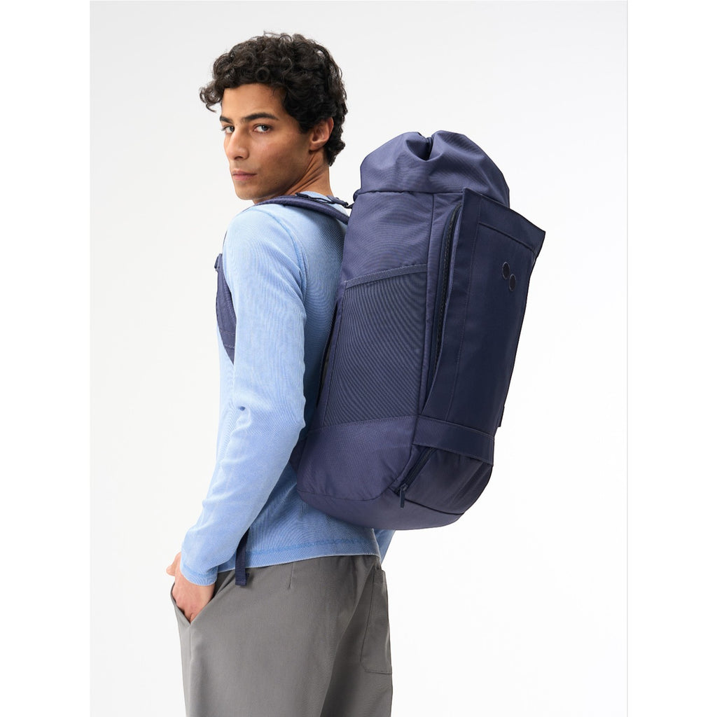Lieblingstasche Blok Large navy blue cylindrical backpack worn by a man in a light blue long-sleeve shirt