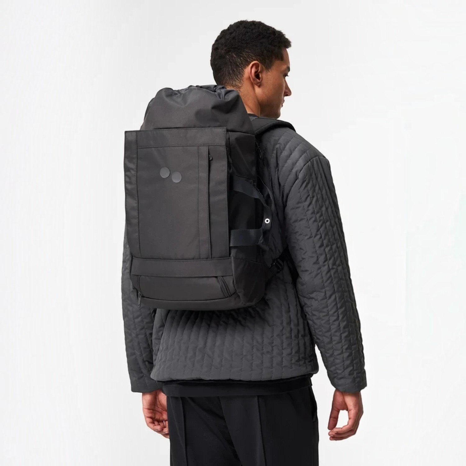 Lieblingstasche Blok Medium backpack in black worn by a man in a quilted jacket, showing the back view.