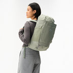 Lieblingstasche Blok Medium sage green backpack worn by a woman, featuring side mesh pockets and a roll-top design.