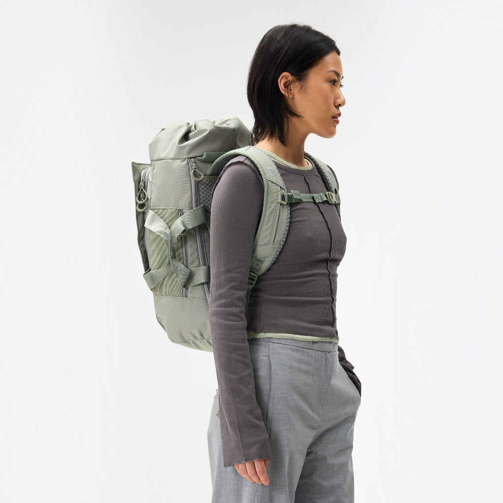 Lieblingstasche Blok Medium sage green backpack worn by a model, featuring a roll-top design and side carry handles.