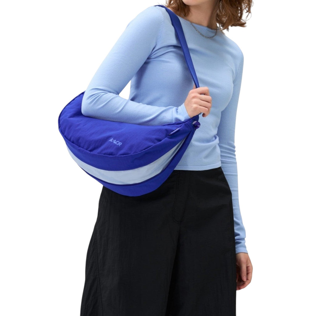 A woman wearing a Lieblingstasche blue crescent-shaped sling bag with a light blue accent stripe over her shoulder.