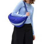 A woman wearing a Lieblingstasche blue crescent-shaped sling bag with a light blue accent stripe over her shoulder.