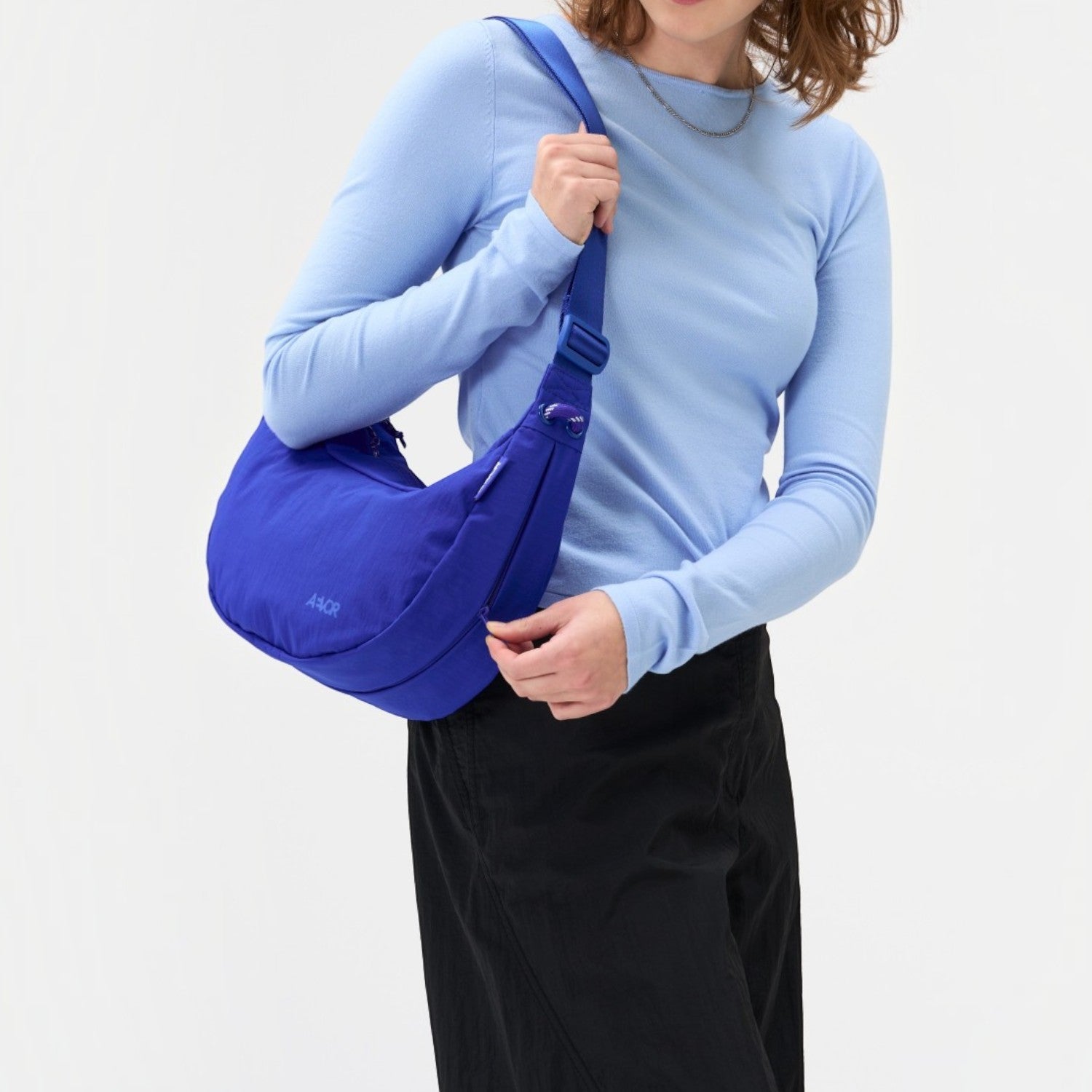 A woman wearing a vibrant blue Lieblingstasche sling bag over her shoulder against a plain white background.