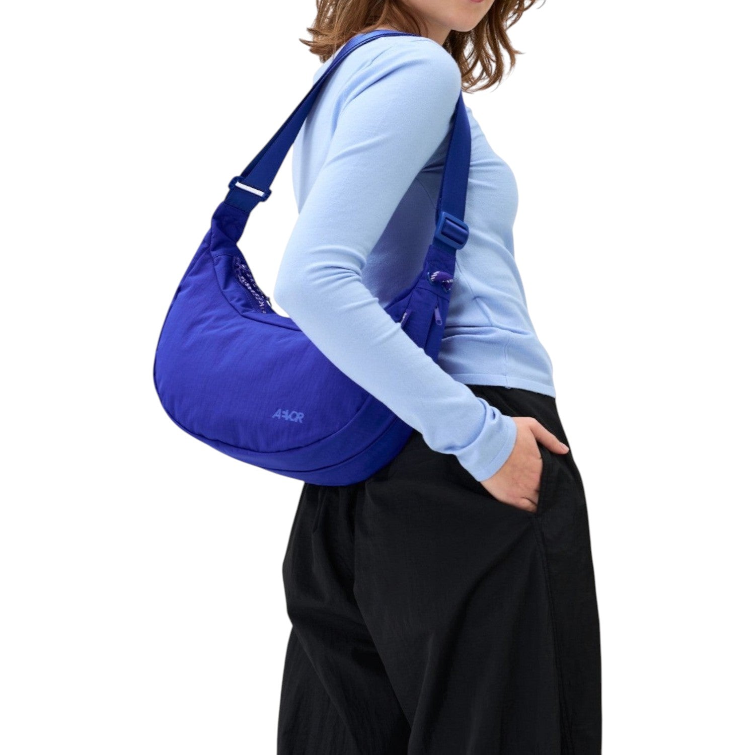 A model wearing a vibrant blue Lieblingstasche sling bag with an adjustable strap against a plain white background.