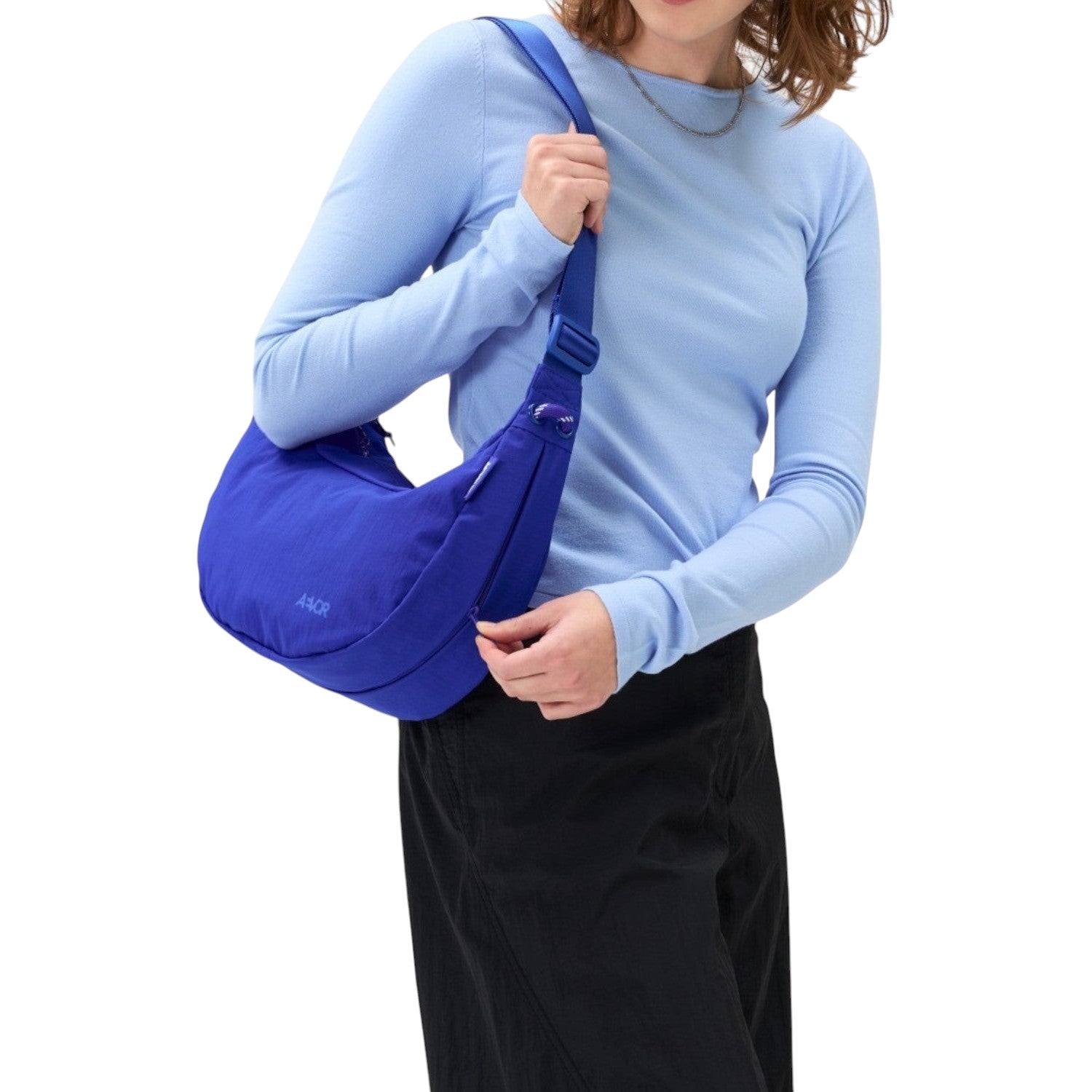 A woman wearing a vibrant blue Lieblingstasche sling bag over her shoulder against a plain white background.