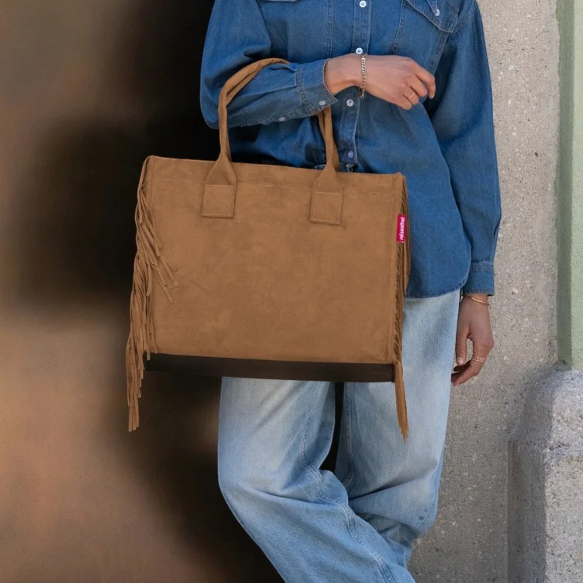 Lieblingstasche Daily Shopper bag in brown suede with fringe details held by a person in denim shirt and jeans