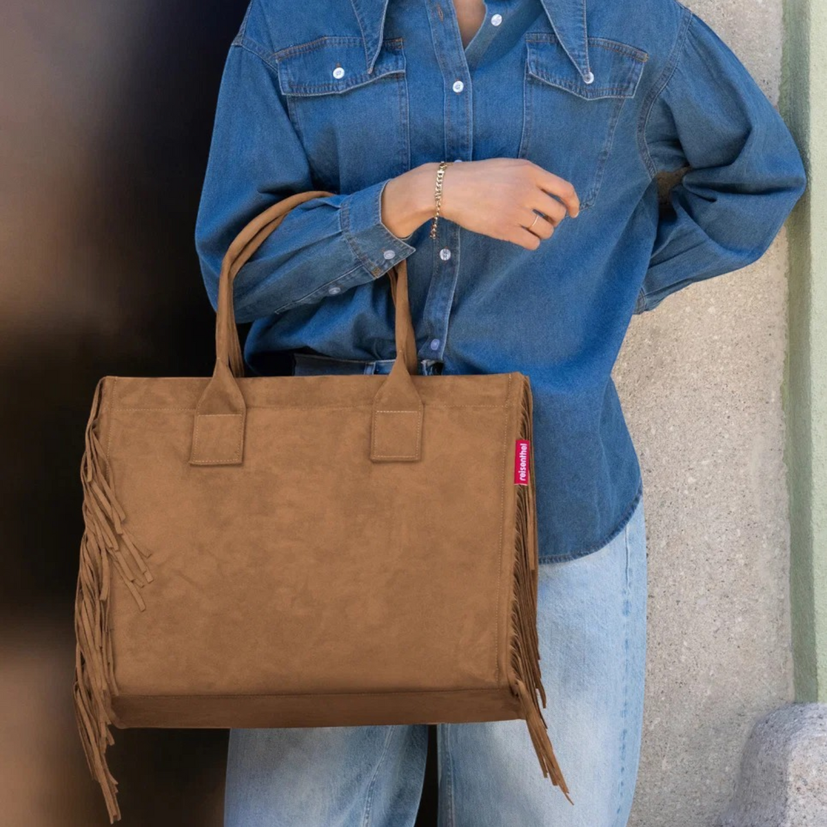 Lieblingstasche Daily Shopper in brown suede with side fringe detail carried by a woman in a denim shirt