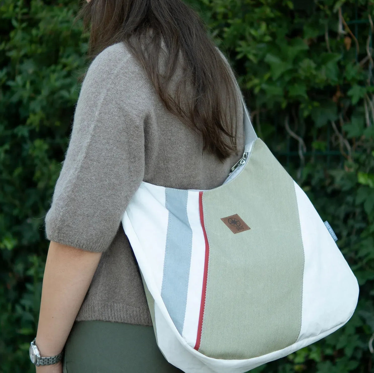 Lieblingstasche Bucht shoulder bag in white, sage green, and blue canvas with a red stripe detail worn by a woman
