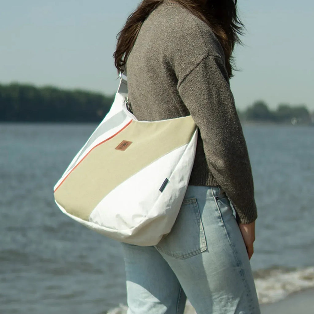 Lieblingstasche Bucht shoulder bag in white and beige with red accents worn by a woman at the beach
