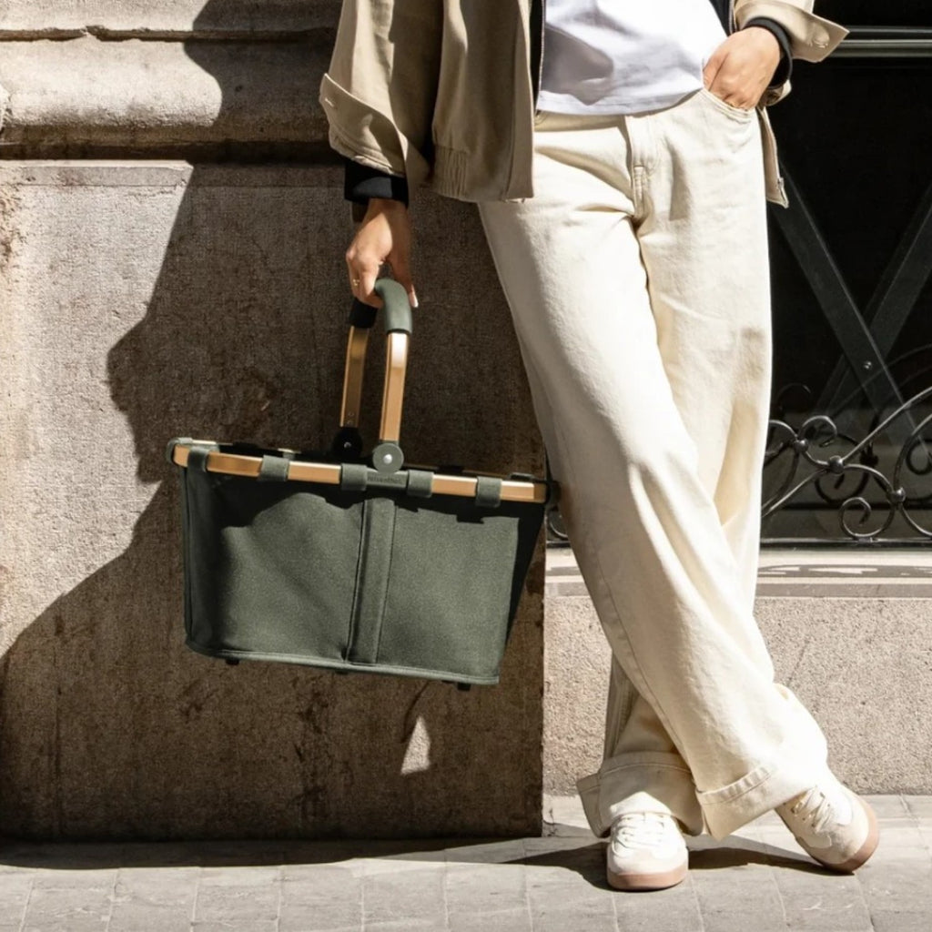 Lieblingstasche carrybag in olive green with a sturdy handle, held by a woman in a beige jacket on a city street.