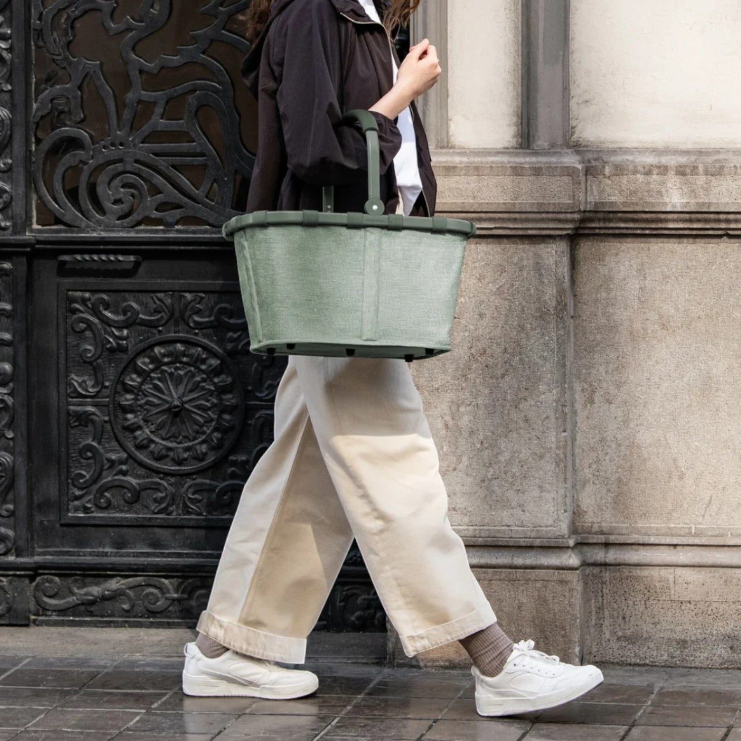 Lieblingstasche Carrybag in sage green with a soft-grip handle, carried by a woman walking on a city street.
