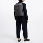 A woman wearing a grey Lieblingstasche Commuter Pack backpack while dressed in a dark navy professional outfit.