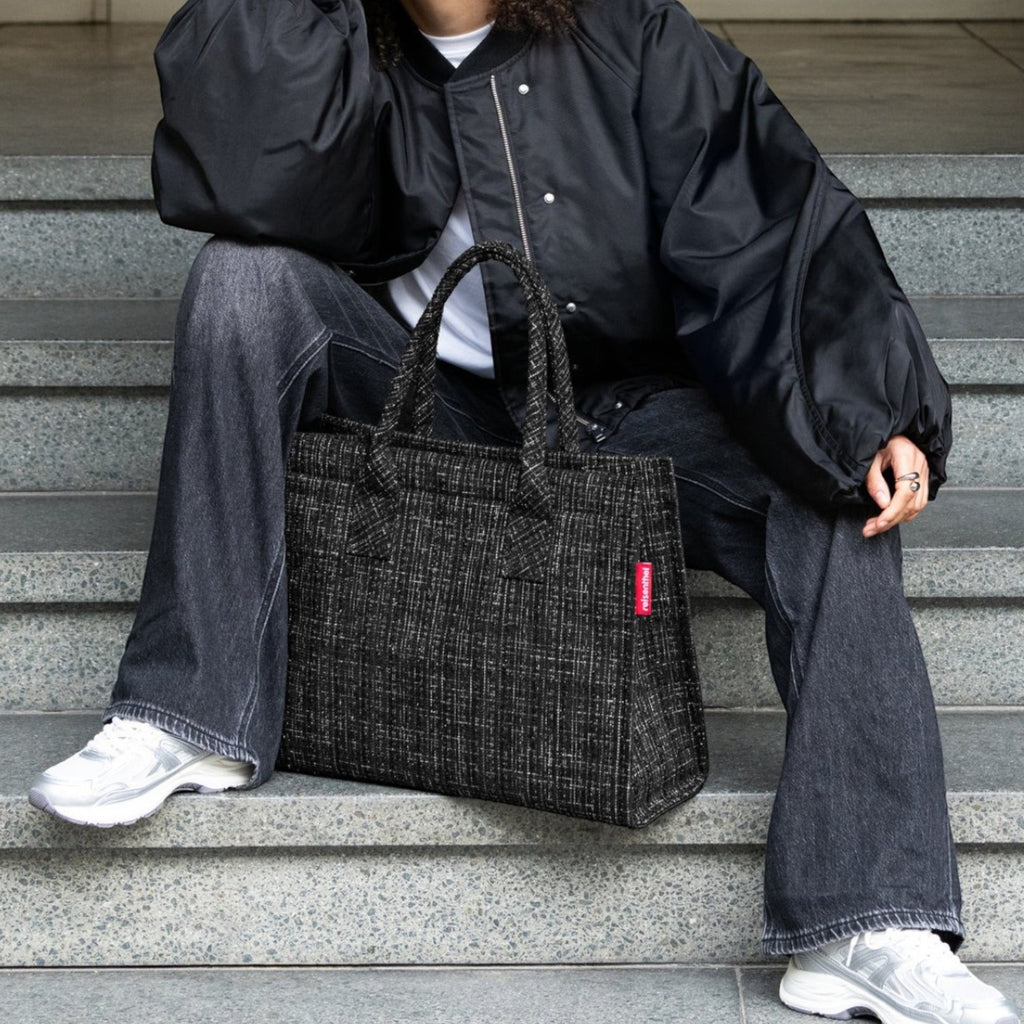 Lieblingstasche Daily Shopper tote bag in black tweed with red logo tag. Model sits on steps.