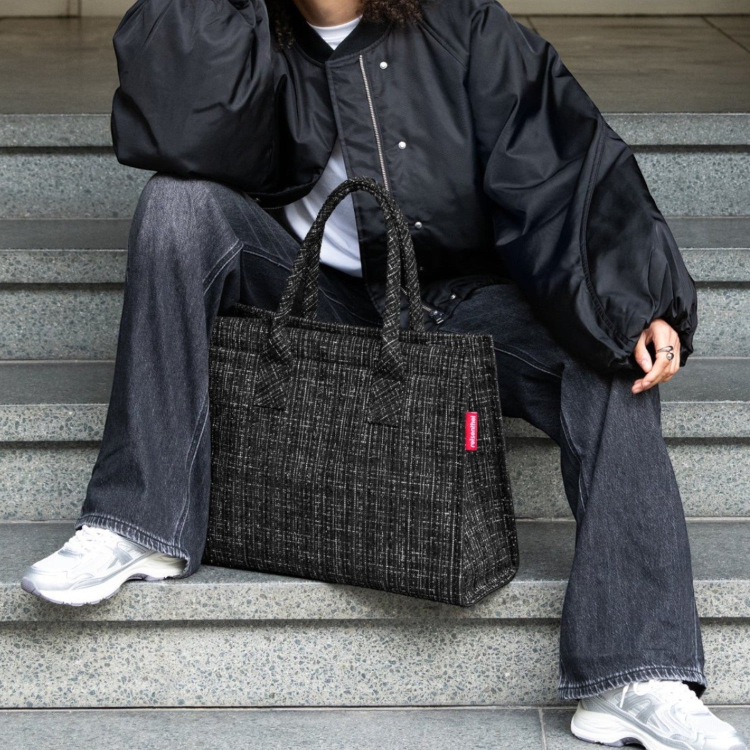 Lieblingstasche Daily Shopper tote bag in black tweed with red logo tag. Model sits on steps.