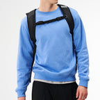A man wearing a black Lieblingstasche Day Pack FLX backpack with adjustable chest straps against a white background.