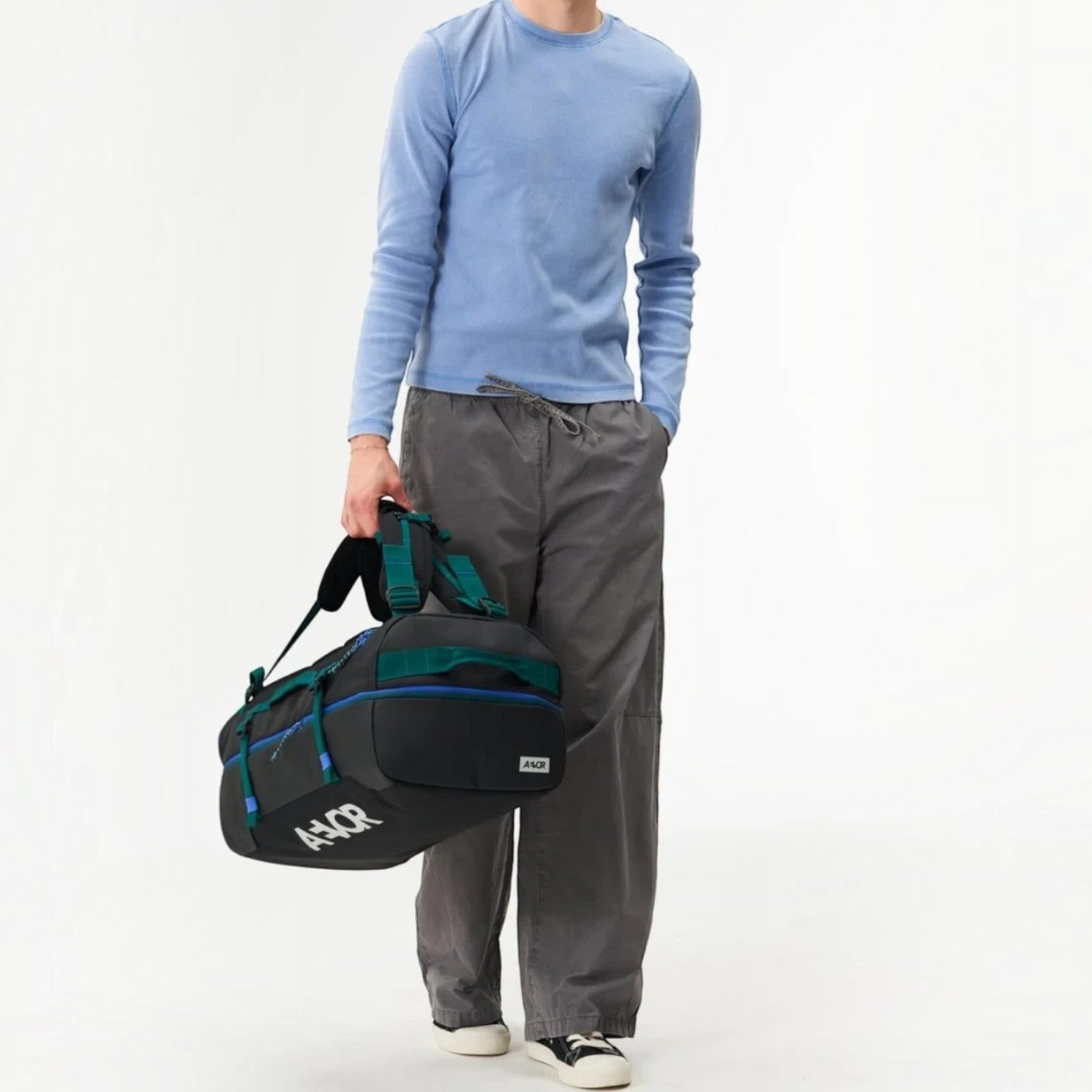 Lieblingstasche Duffel Pack in black with teal accents, held by a model wearing a light blue shirt and grey trousers.