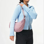 A model wearing a Lieblingstasche dusty pink crescent-shaped sling bag over a light blue ribbed zip-up sweater.
