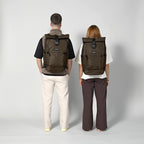 Lieblingstasche eoto Tall41 brown rolltop travel backpack worn by a man and woman against a light grey background