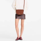 Model wearing a brown leather Lieblingstasche Epure Umhängetasche M crossbody bag with a white sweater and skirt