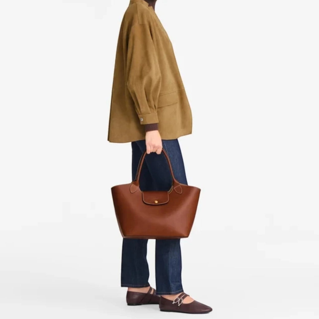 Lieblingstasche Epure Schultertasche L in brown leather held by a model wearing a tan jacket and dark jeans
