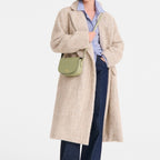 Lieblingstasche Epure S light green leather crossbody bag with gold hardware worn by a woman in a beige coat.