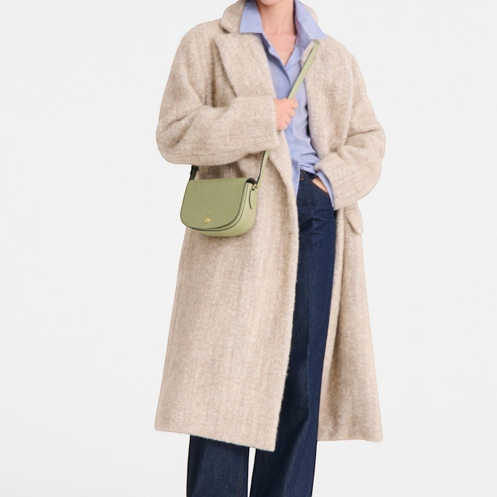 Lieblingstasche Epure S light green leather crossbody bag with gold hardware worn by a woman in a beige coat.