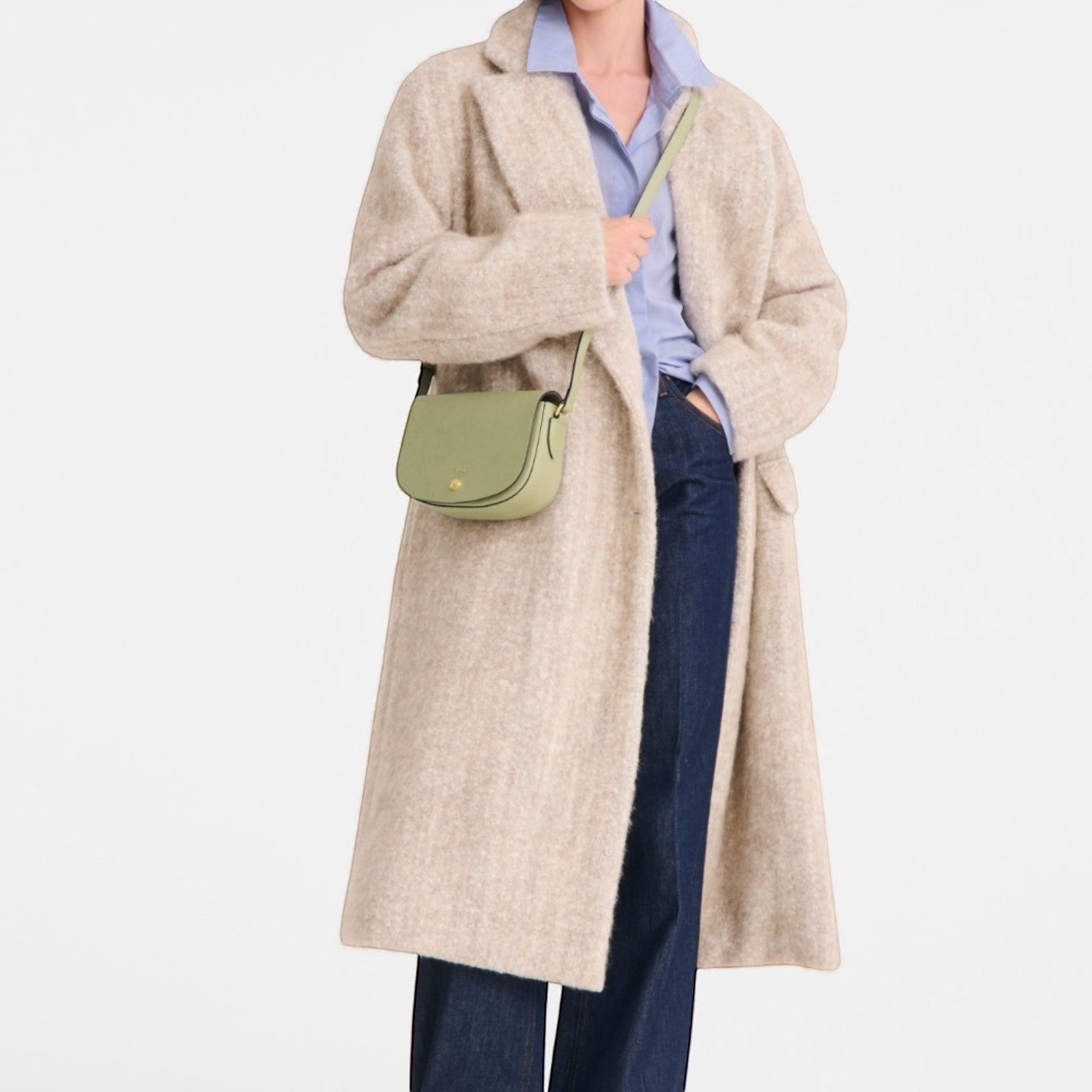 Lieblingstasche Epure S light green leather crossbody bag with gold hardware worn by a woman in a beige coat.