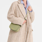 Lieblingstasche Epure S light green leather crossbody bag with gold hardware worn by a model in a beige coat.