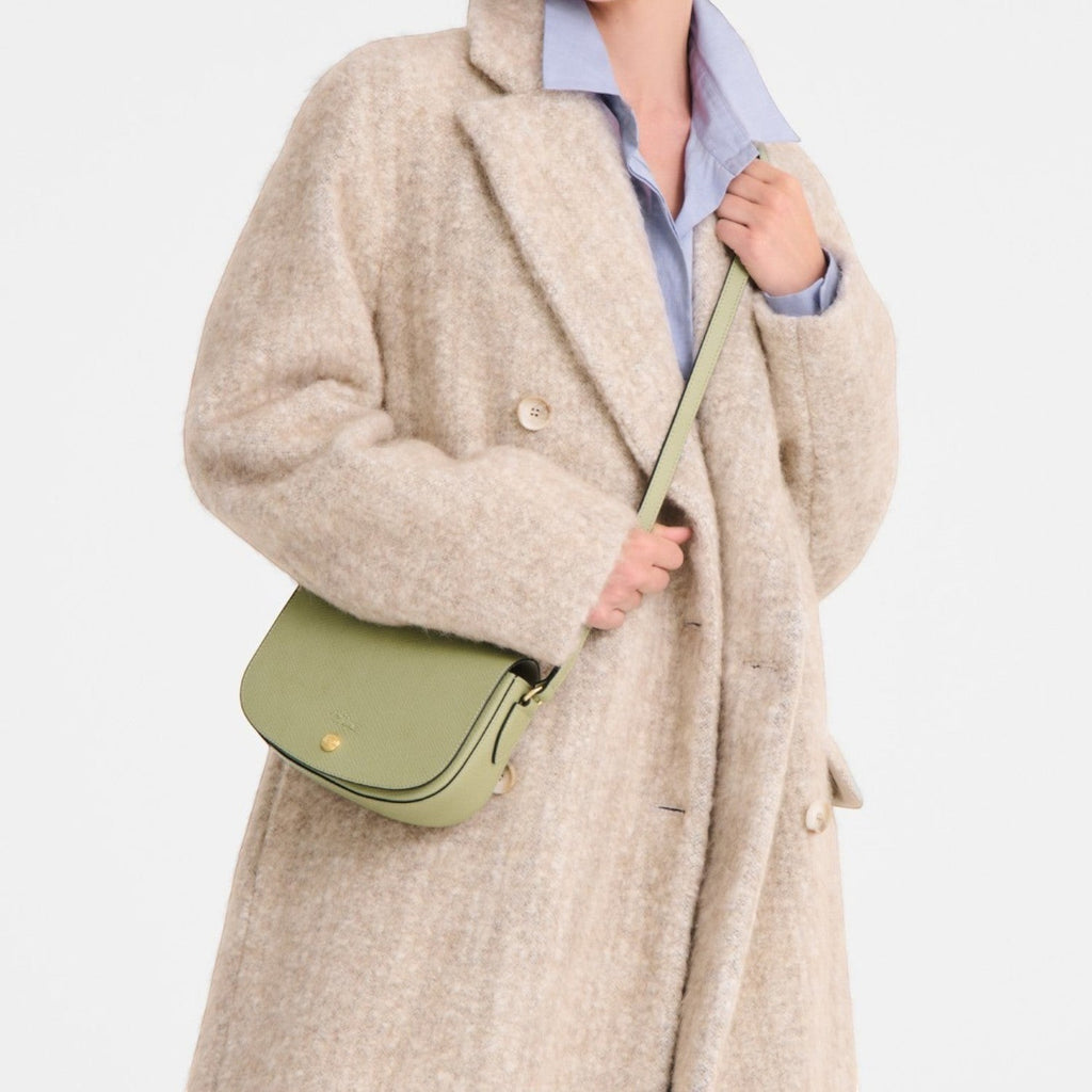 Lieblingstasche Epure S light green leather crossbody bag with gold hardware worn by a model in a beige coat.