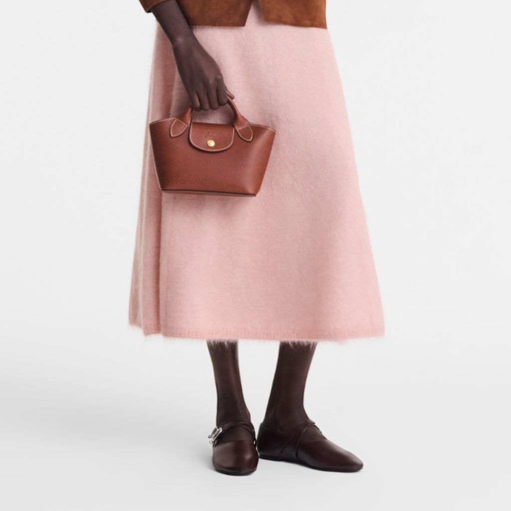 Lieblingstasche Epure XS brown leather handbag with top handle and gold clasp, worn by a model in a brown suede jacket and pink skirt.