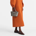 Lieblingstasche Epure XS grey leather handbag with top handle and flap closure, worn by a model in an orange dress.